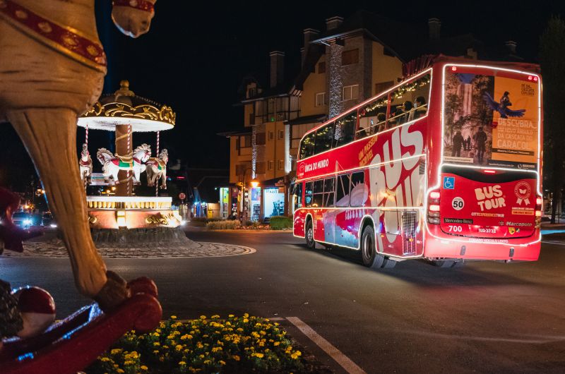 Ônibus do Bustour Illumination Show passando pelo carrossel iluminado no centro de Canela
