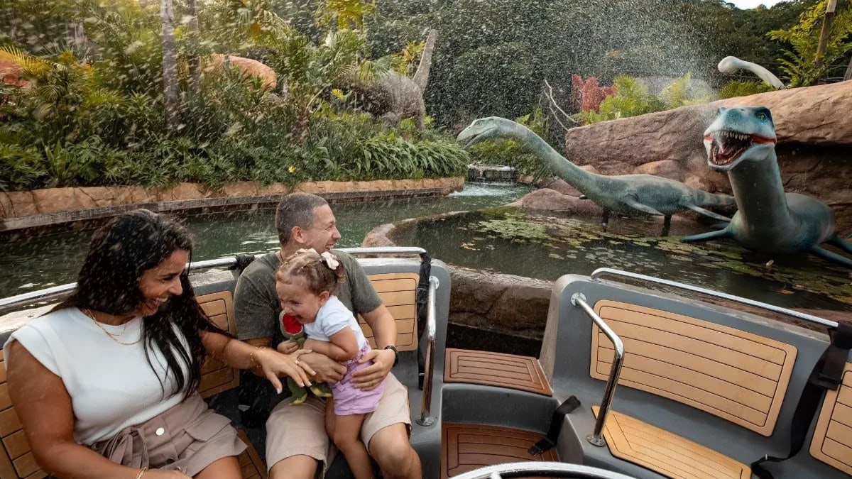 Una familia en el paseo en barco de «Aventura Jurásica», pasando entre dinosaurios