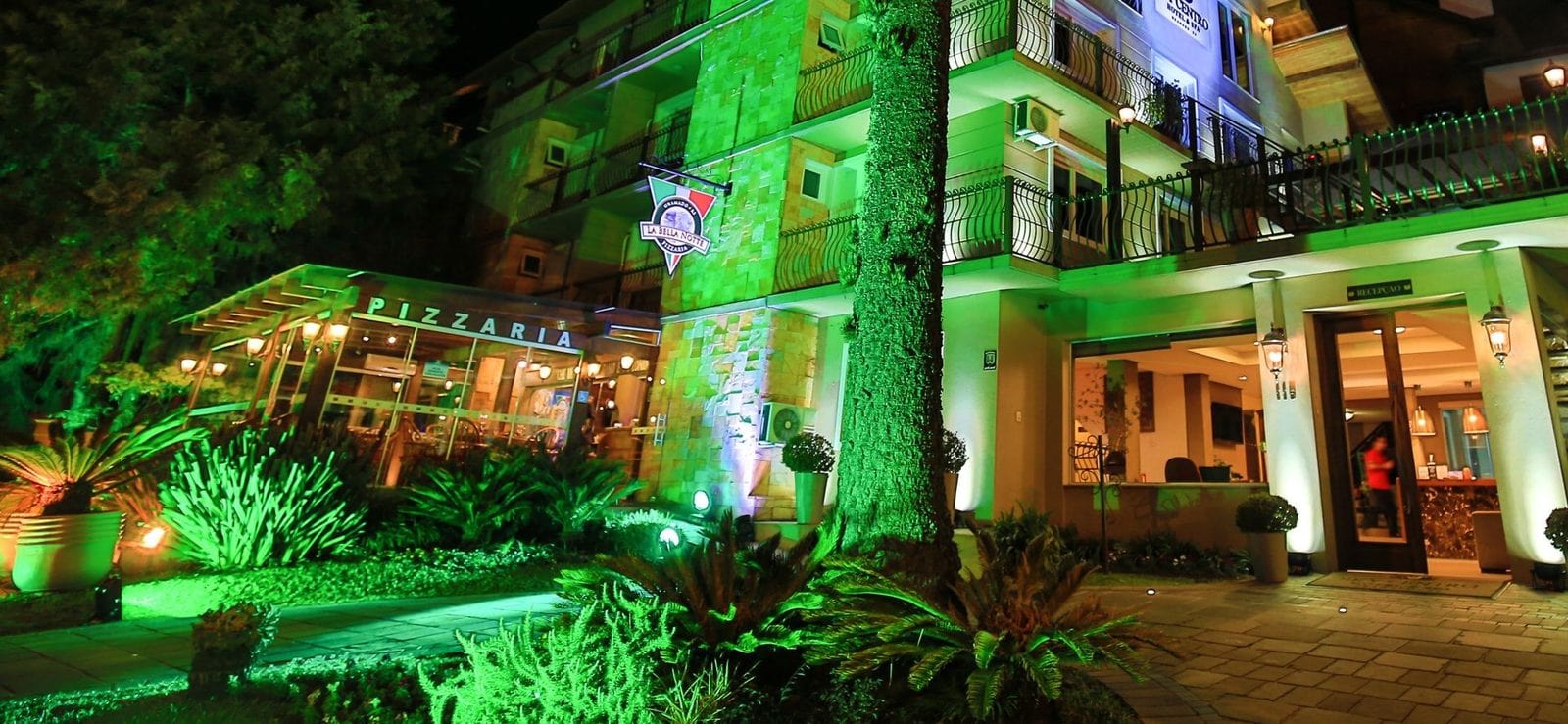 Entrada da La Bella Notte Pizzaria com iluminação verde, no centro de Gramado