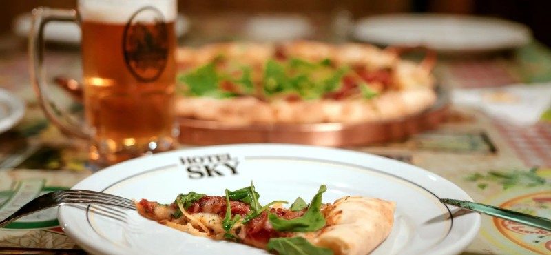 Fatia de pizza e chopp artesanal na mesa da La Bella Notte Pizzaria, em Gramado