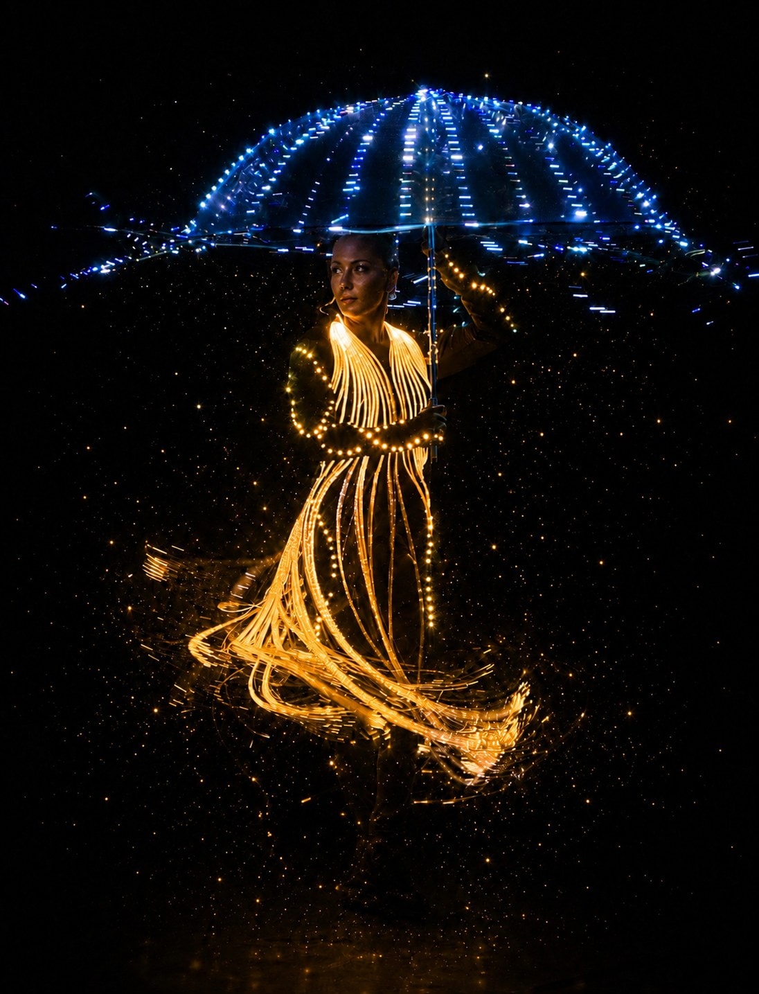 Bailarina com figurino dourado de LED e guarda-chuva de luz azul no espetáculo O Brilho do Natal em Gramado
