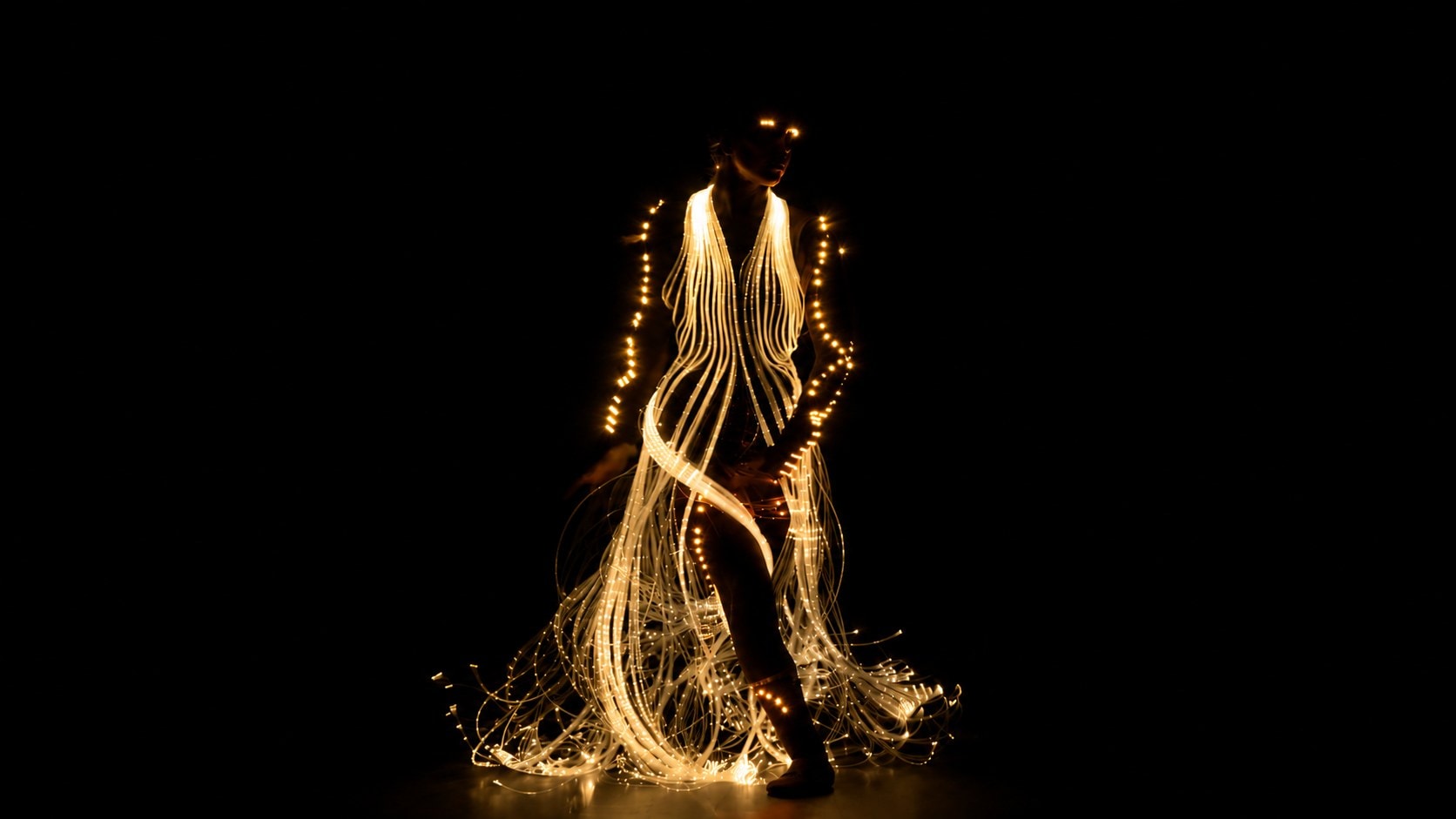 Bailarina com vestido de luz dourada no escuro no espetáculo O Brilho do Natal, Natal Luz Gramado 2026