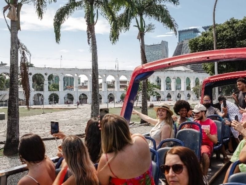 Passageiros no andar aberto do Rio Samba Bus com os Arcos da Lapa ao fundo, Rio de Janeiro