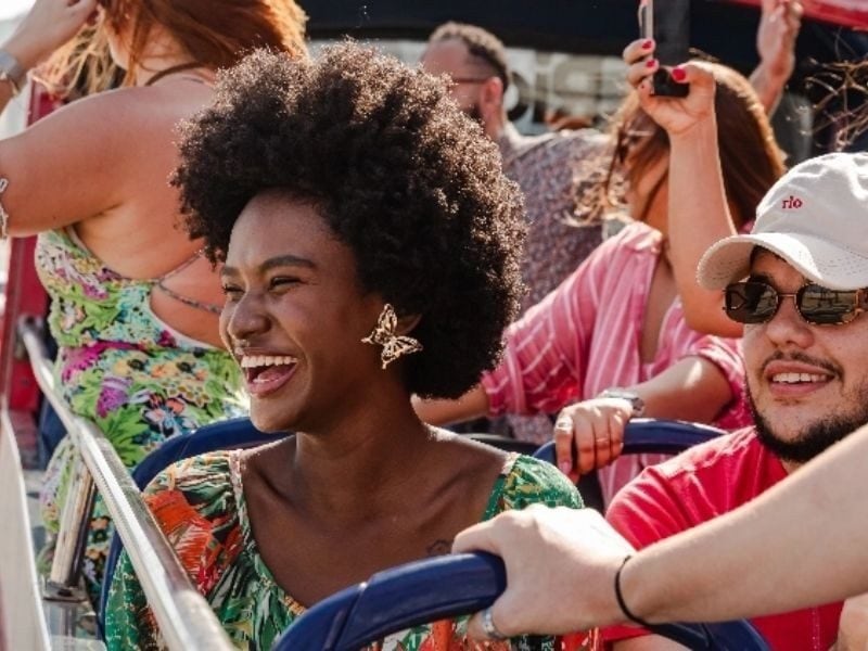 Turistas sorrindo no andar aberto do Rio Samba Bus, city tour panorâmico no Rio de Janeiro