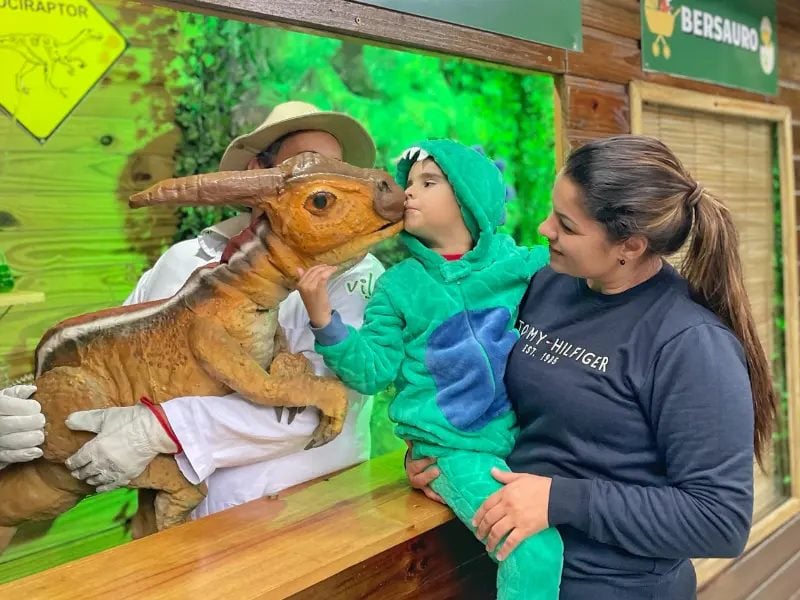 Bebê dinossauro do Laboratório Encantado interagindo com criança na Vila Encantada, Pomerode-SC