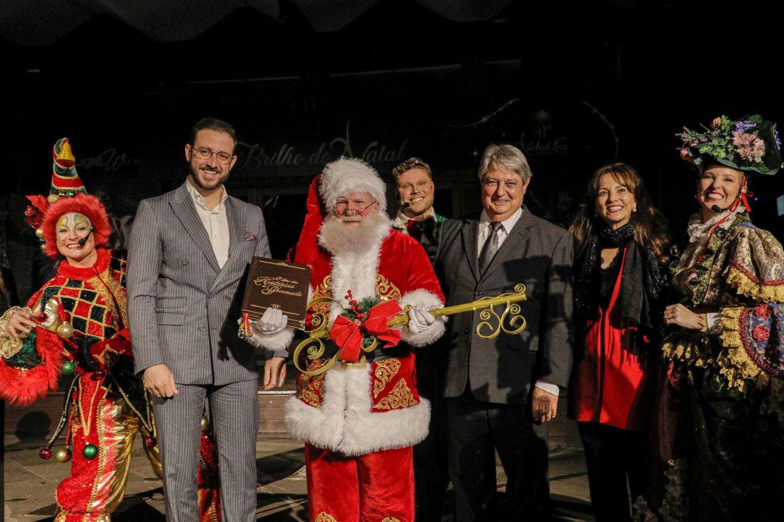 Papai Noel segura a chave da cidade e o Livro das Histórias de Gramado ao lado de autoridades e personagens da Trupe de Natal