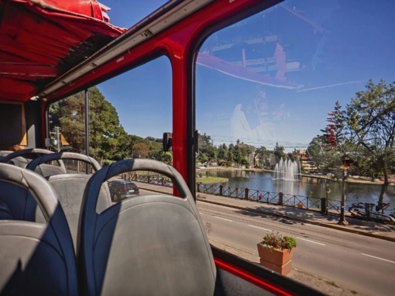 Andar superior aberto do Bustour com vista para lago em dia de sol