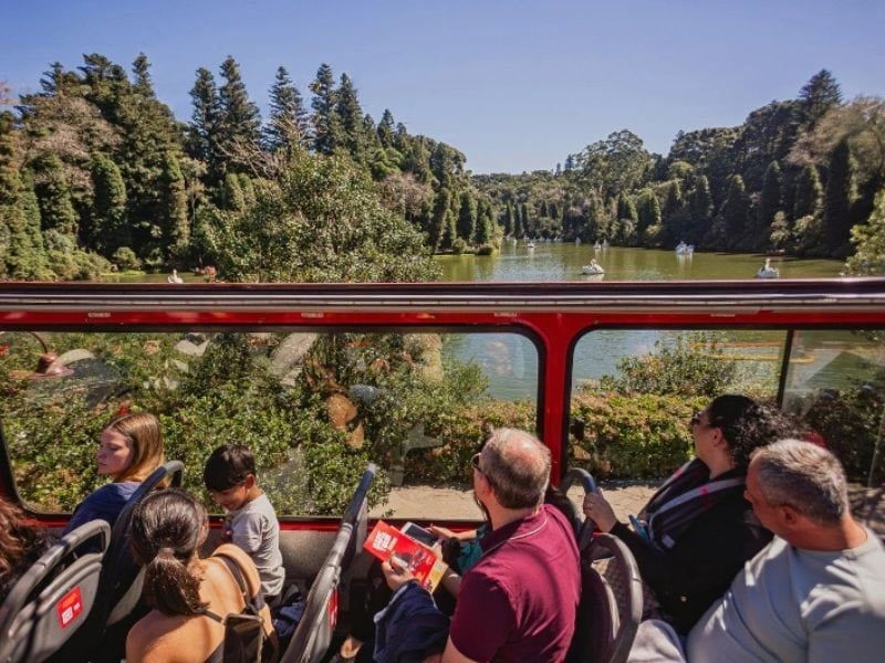 Passageiros no andar superior do Bustour com vista para lago na Serra Gaúcha