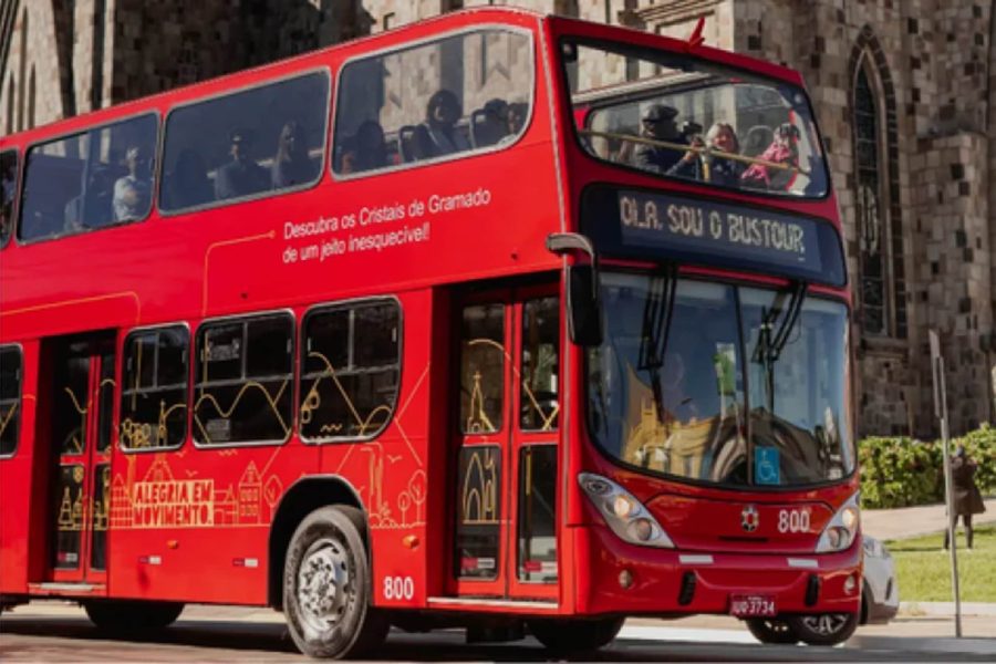 Ônibus vermelho de dois andares do Bustour em frente à Catedral de Pedra, em Canela