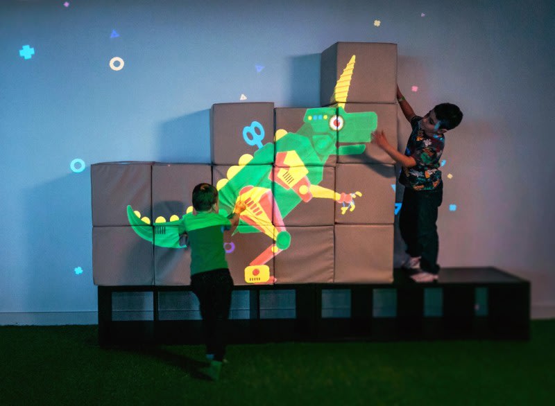 Crianças montando blocos com projeção de dinossauro no Hello Park, em São Paulo