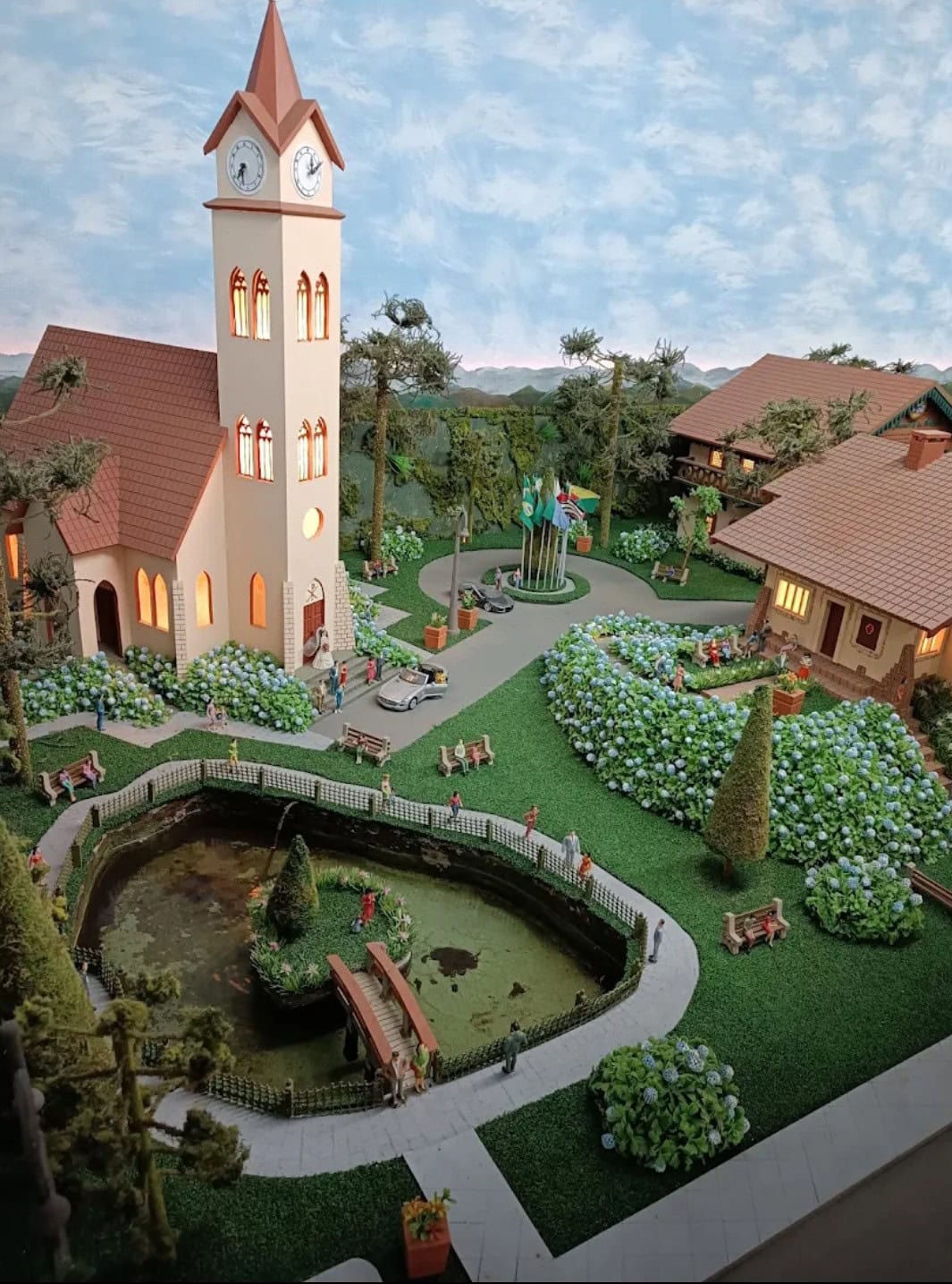 Praça em miniatura com igreja de torre do relógio e lago no Mundo Encantado em Gramado