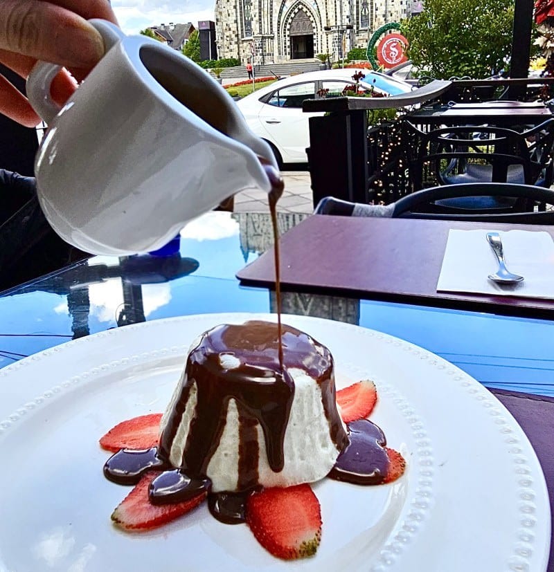 Calda de chocolate sendo servida sobre a sobremesa com a Catedral de Pedra ao fundo no Otto Bistrot em Canela