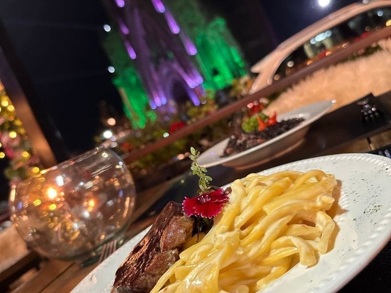Massa com carne no jantar do Otto Bistrot com a Catedral de Pedra iluminada ao fundo em Canela