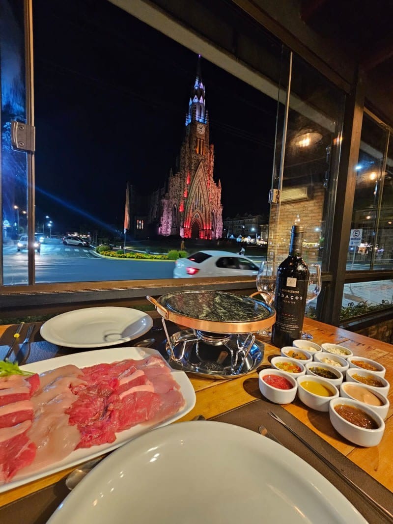 Mesa de fondue do Sello Restaurante com vista para a Catedral de Pedra iluminada em Canela