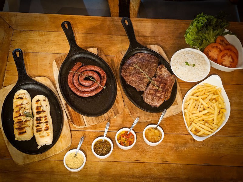 Carnes na brasa, linguiça e acompanhamentos servidos em frigideiras de ferro no Sello Restaurante
