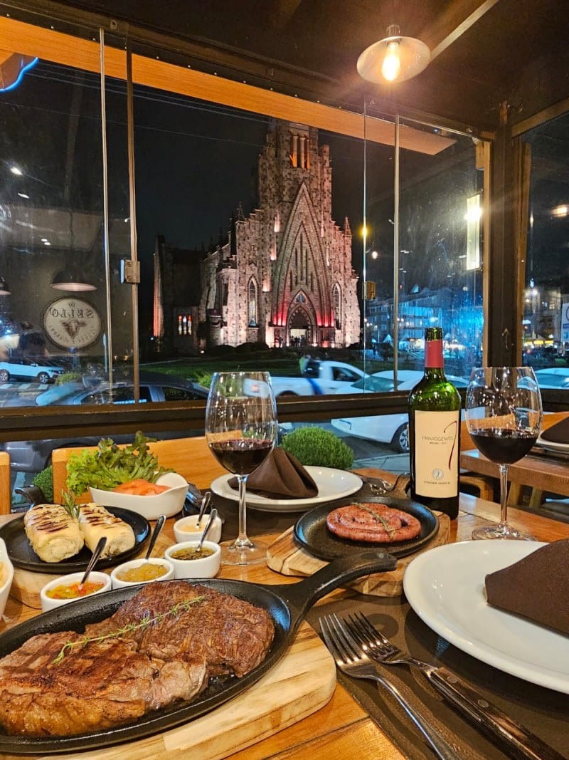 Corte de carne na pedra com a Catedral de Pedra vista pela janela do Sello Restaurante