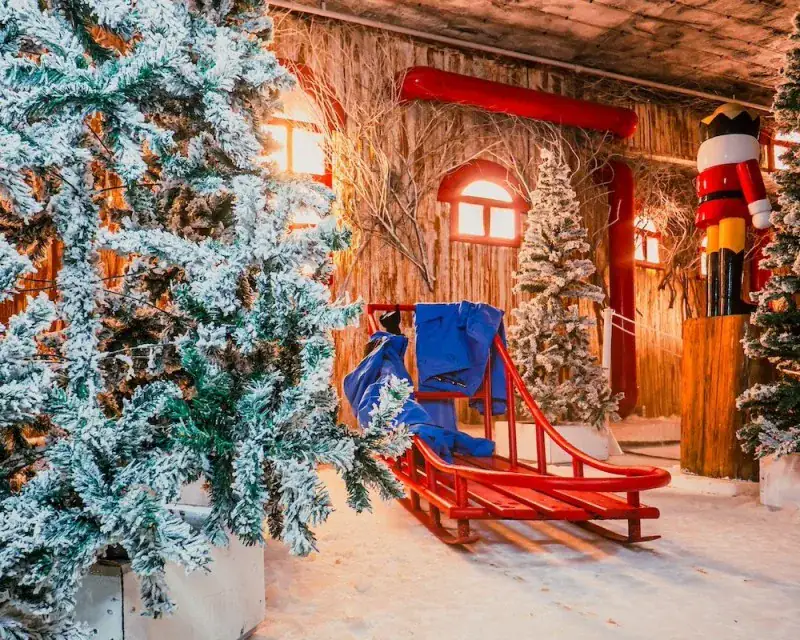 Trenó vermelho entre pinheiros com neve cenográfica na Aldeia do Papai Noel, em Gramado