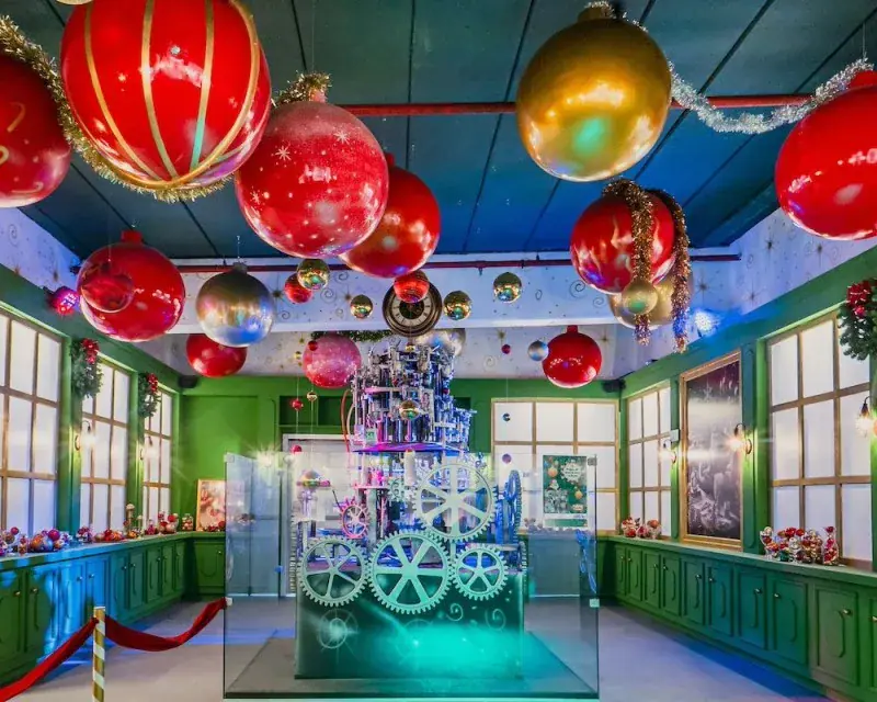 Sala com bolas de Natal gigantes penduradas no teto e máquina de engrenagens na Aldeia do Papai Noel, em Gramado