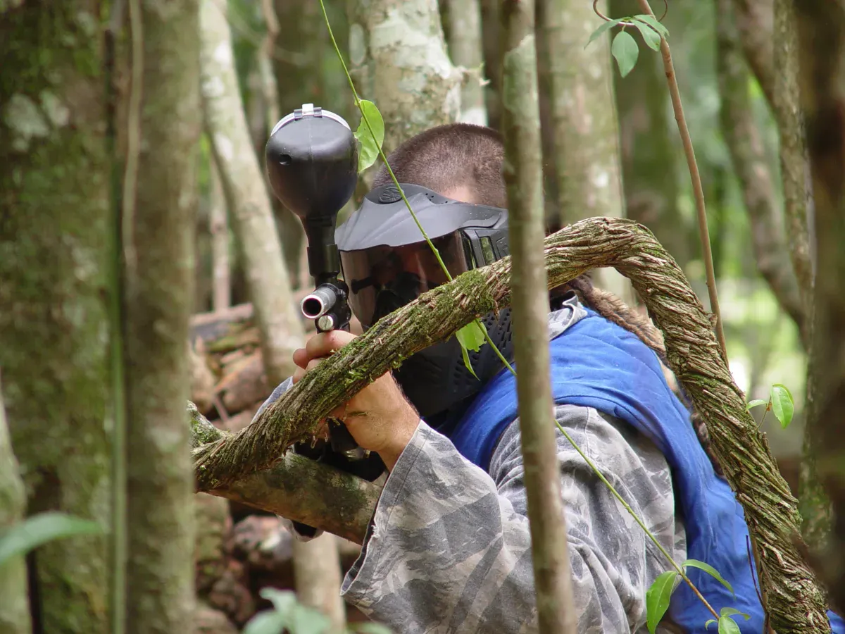 Jogador de paintball com máscara mirando entre árvores da mata no Brasil Raft Park, em Três Coroas