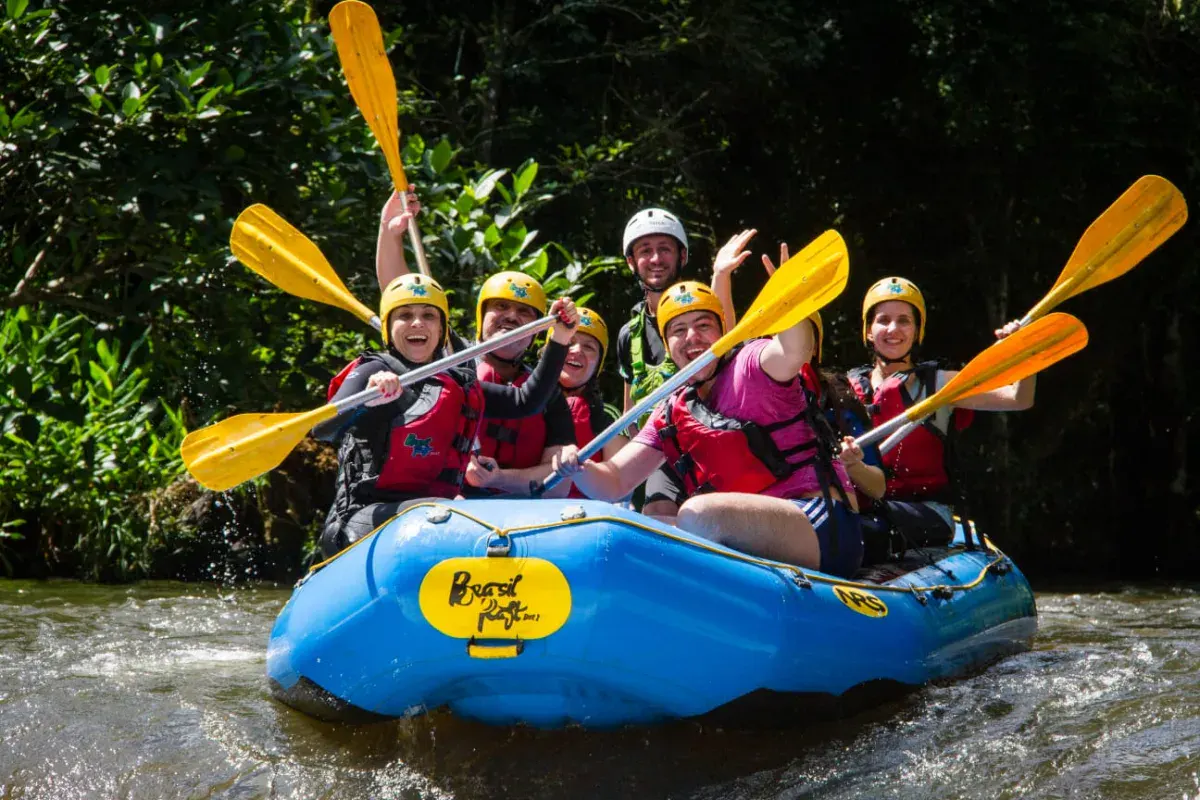 Grupo sorridente levantando os remos em bote do Brasil Raft Park, no Rio Paranhana, em Três Coroas