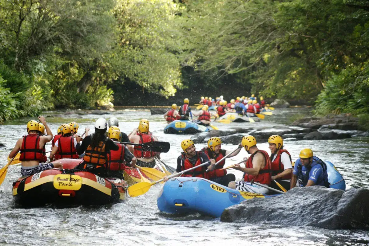 Vários botes de rafting com participantes de capacete e colete no Rio Paranhana, em Três Coroas