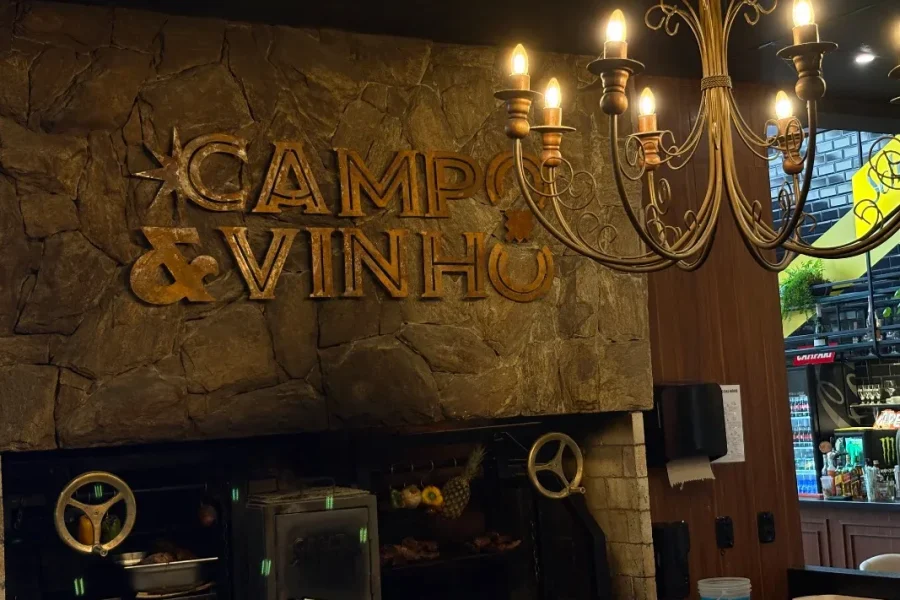Carnes grelhando na parrilla sob o letreiro do Campo & Vinho, em Gramado