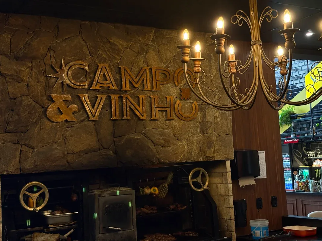 Carnes grelhando na parrilla sob o letreiro do Campo & Vinho, em Gramado