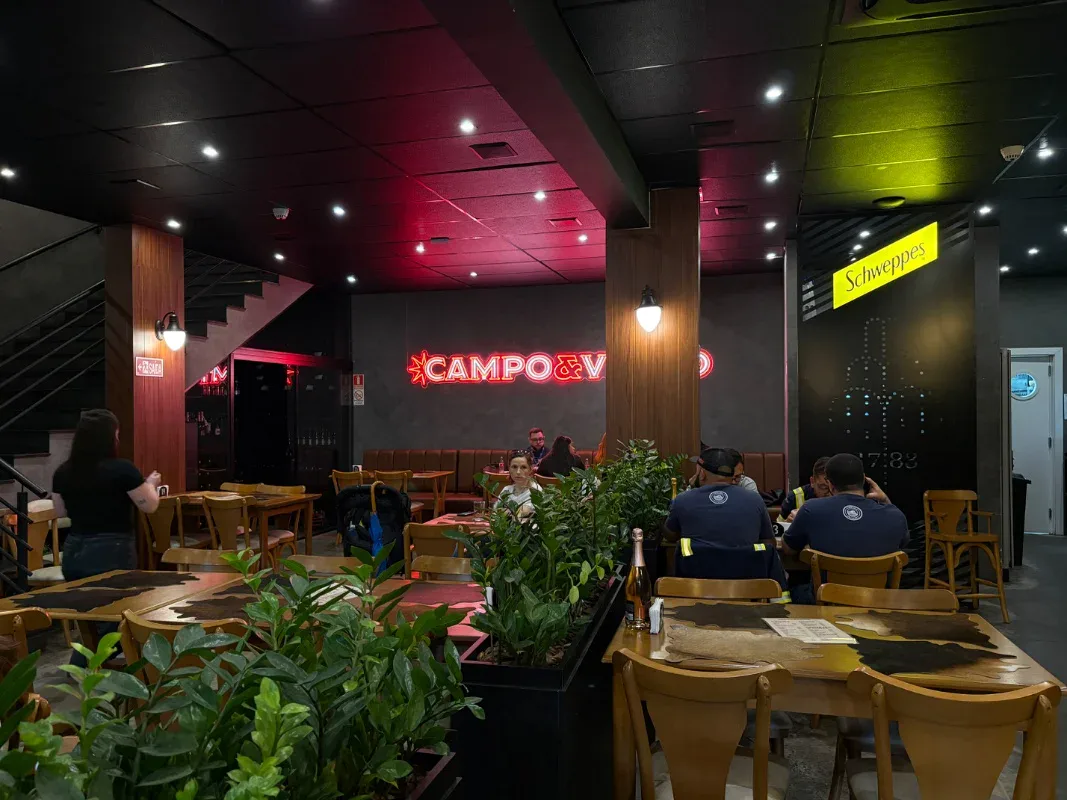 Salão do restaurante Campo & Vinho, na Rua Coberta de Gramado, com mesas de madeira e letreiro em neon