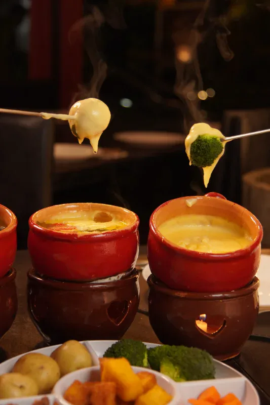 Batata e brócolis mergulhados no fondue de queijo do Caquelon Fondue, em Canela