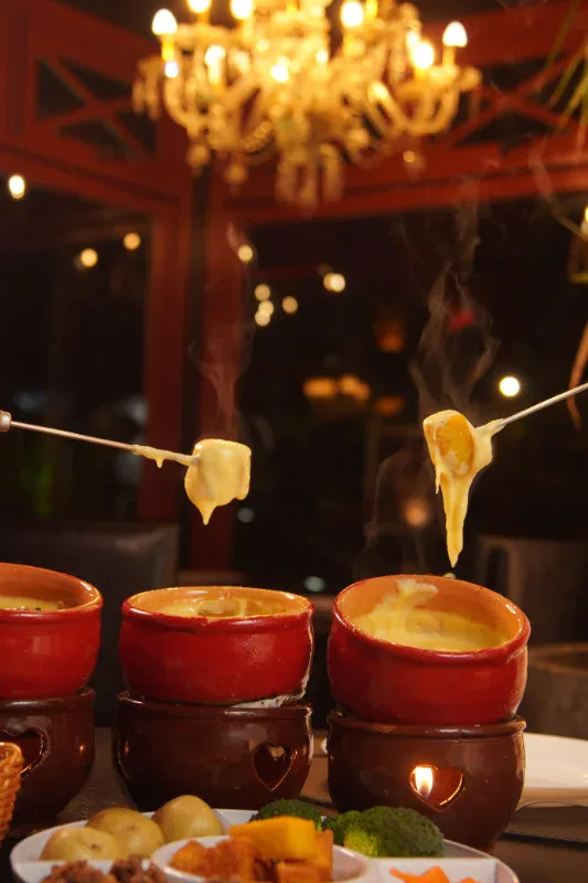 Três panelinhas de fondue de queijo sob lustre no salão do Caquelon Fondue, em Canela