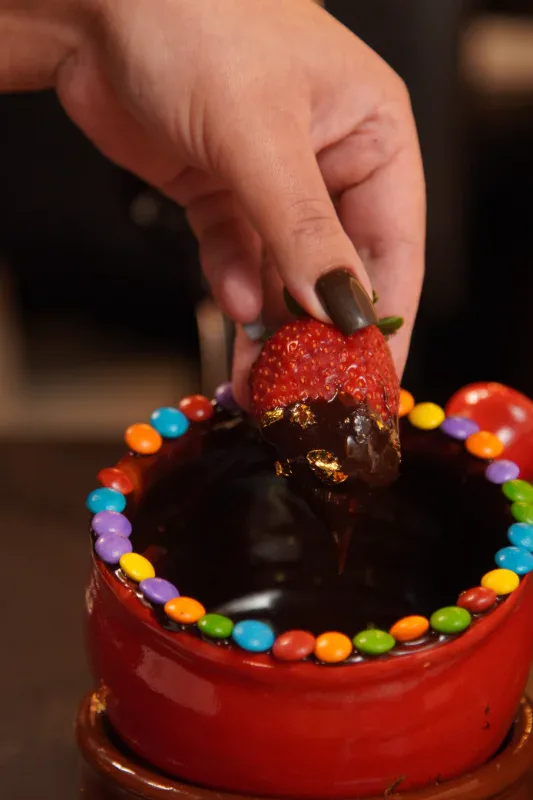 Morango coberto de chocolate ao leite com confeitos coloridos no Caquelon Fondue, em Canela
