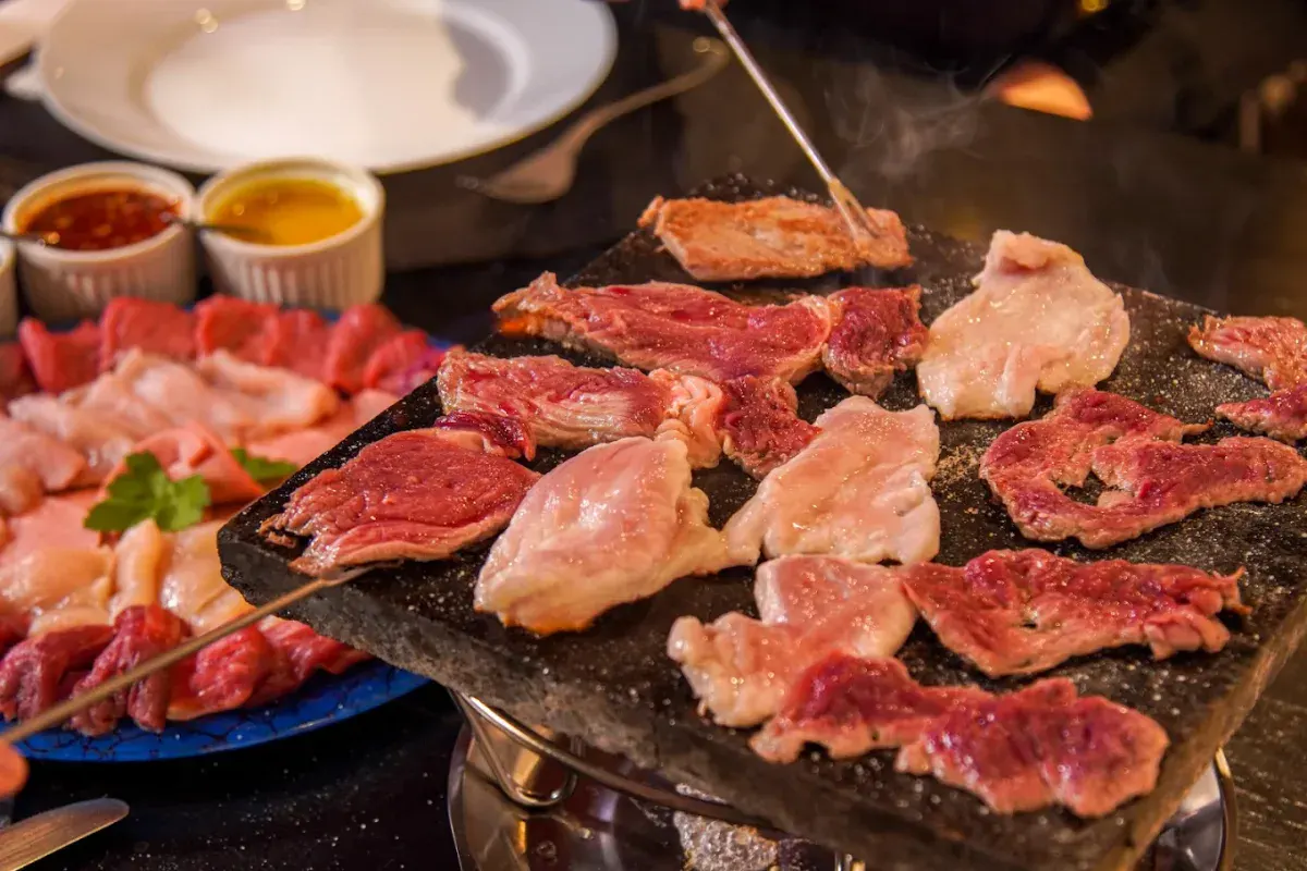 Carnes grelhando na pedra com molhos na sequência de fondue do Caquelon Fondue, em Canela-RS