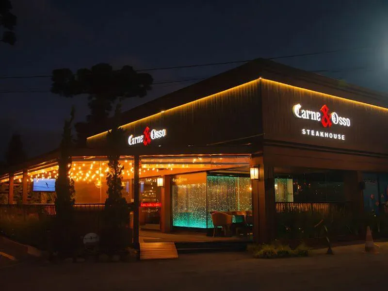 Fachada iluminada à noite do Carne & Osso Steakhouse, na Av. das Hortênsias, em Gramado
