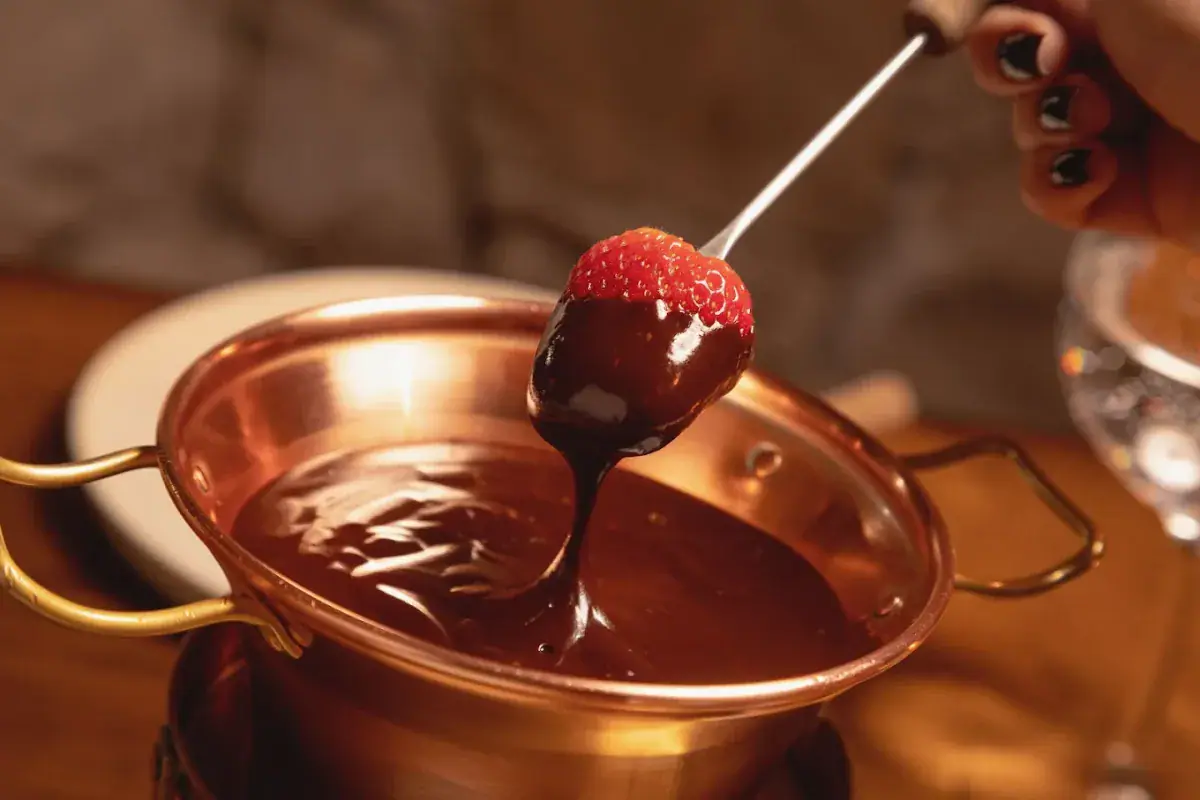 Morango coberto de chocolate saindo da panela de cobre do fondue doce do Chalezinho, em Gramado