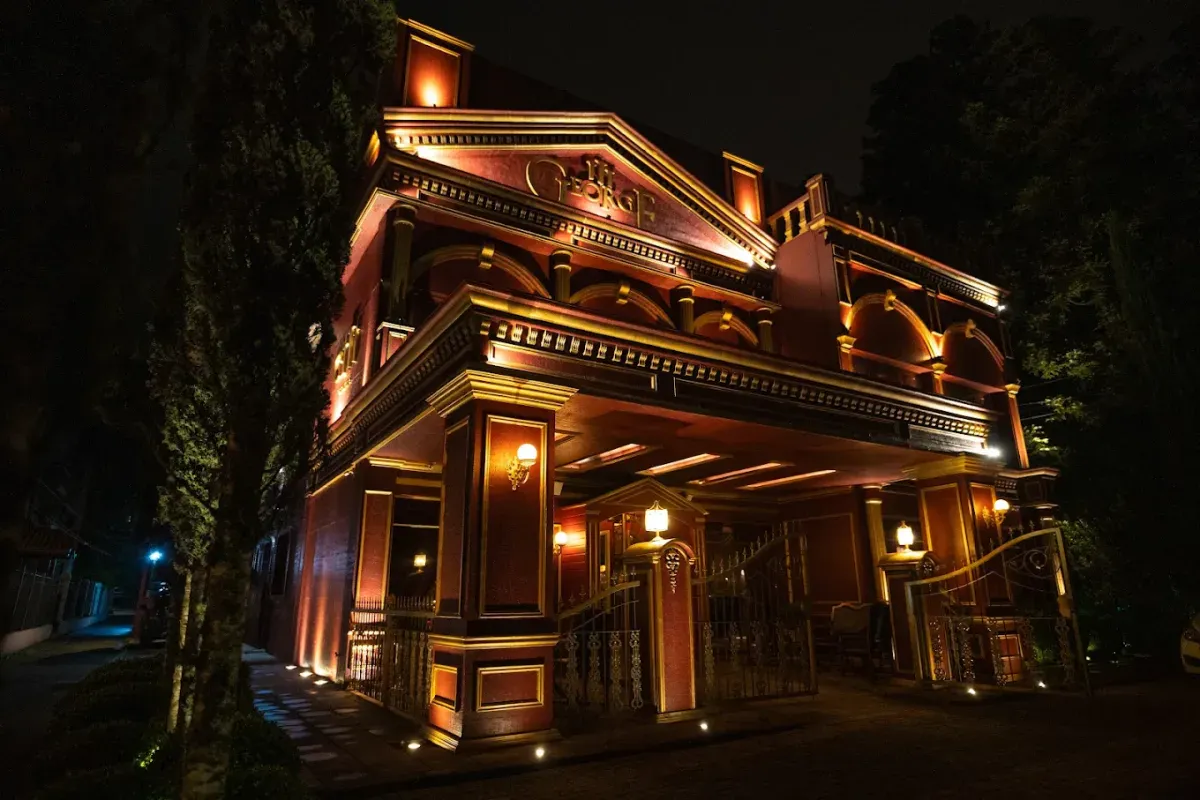 Prédio do George III iluminado em vermelho e dourado à noite, visto da calçada, em Gramado