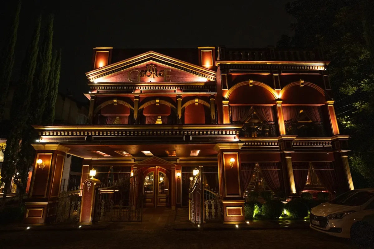 Fachada iluminada do restaurante George III à noite, com colunas e arcos em estilo de palácio, em Gramado