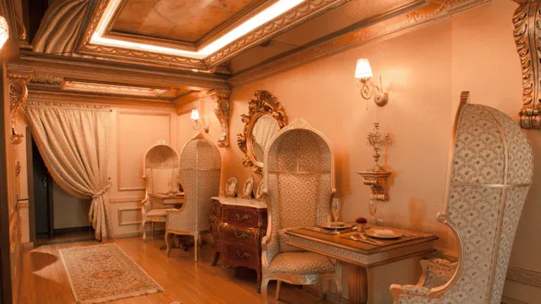 Sala privativa do George III com poltronas de encosto alto, espelho dourado e mesa posta para dois, em Gramado