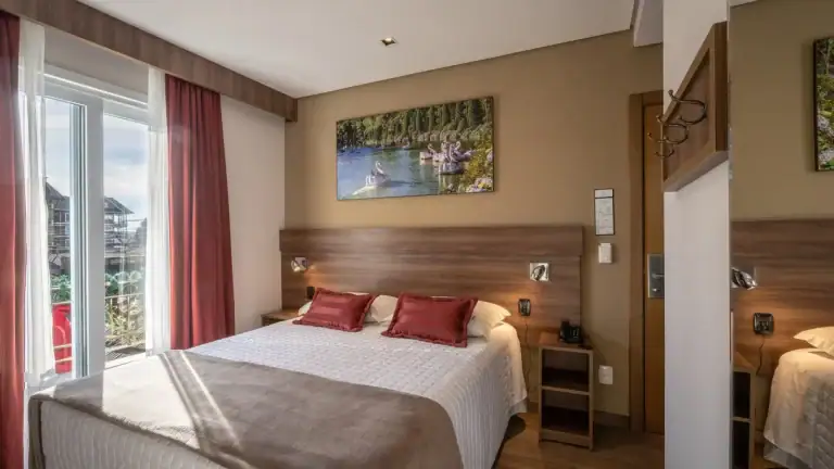 Quarto de casal com almofadas vermelhas e janela ampla em hotel Fioreze, em Gramado