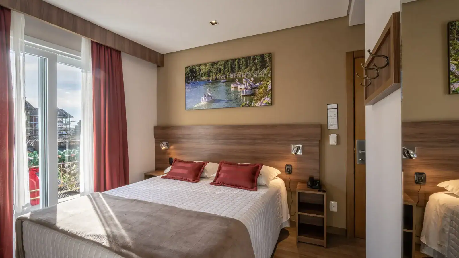 Quarto de casal com almofadas vermelhas e janela ampla em hotel Fioreze, em Gramado