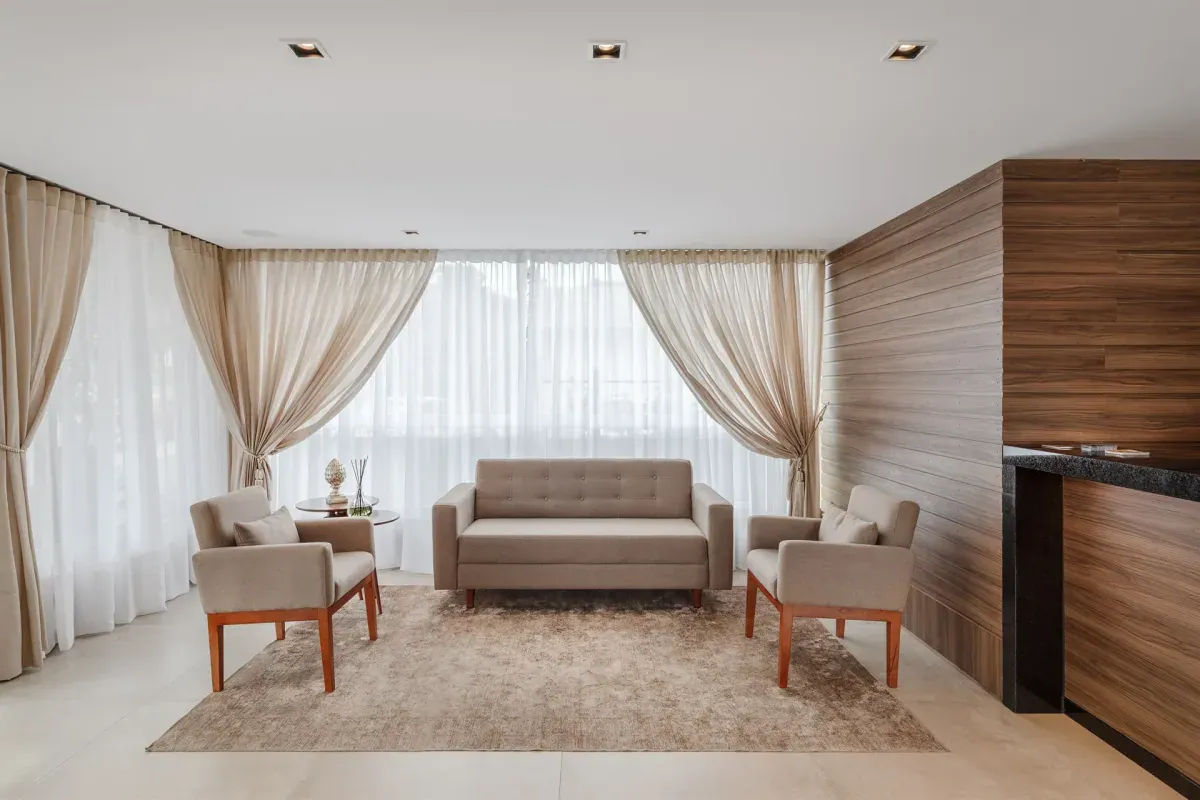 Sala de estar com sofá, poltronas e cortinas claras no Hotel Fioreze Primo, em Gramado