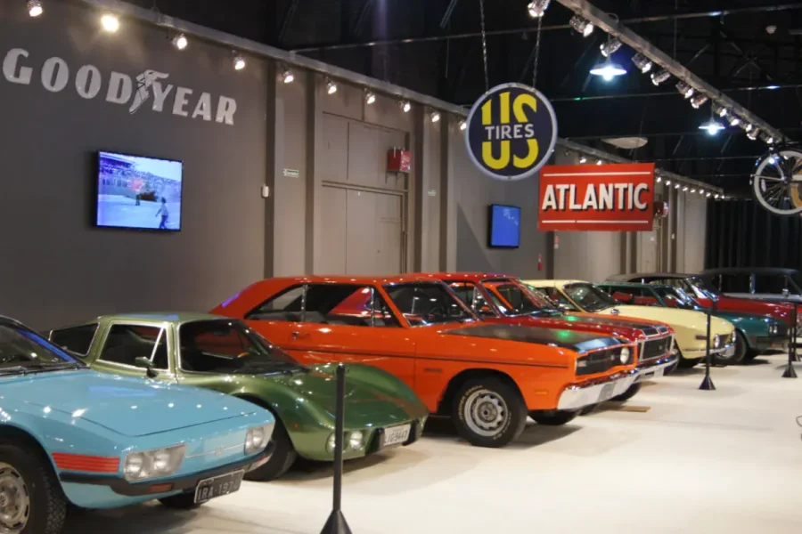 Carros clássicos enfileirados sob placas antigas de Goodyear e Atlantic no Museu do Automóvel de Canela