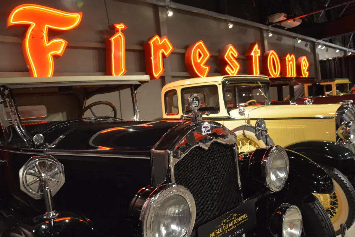 Carros antigos dos anos 1920 sob letreiro neon da Firestone no Museu do Automóvel de Canela