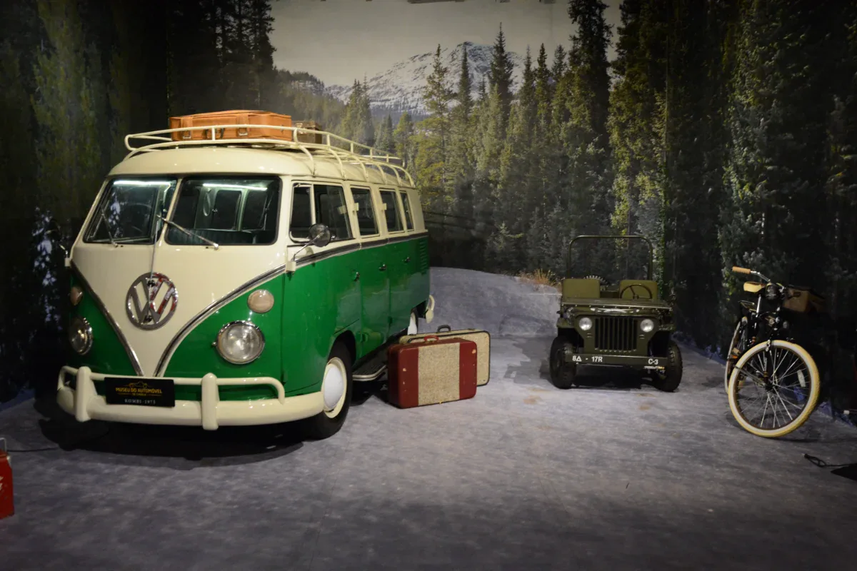 Kombi verde e branca, jipe militar e bicicleta antiga em cenário de floresta no Museu do Automóvel de Canela
