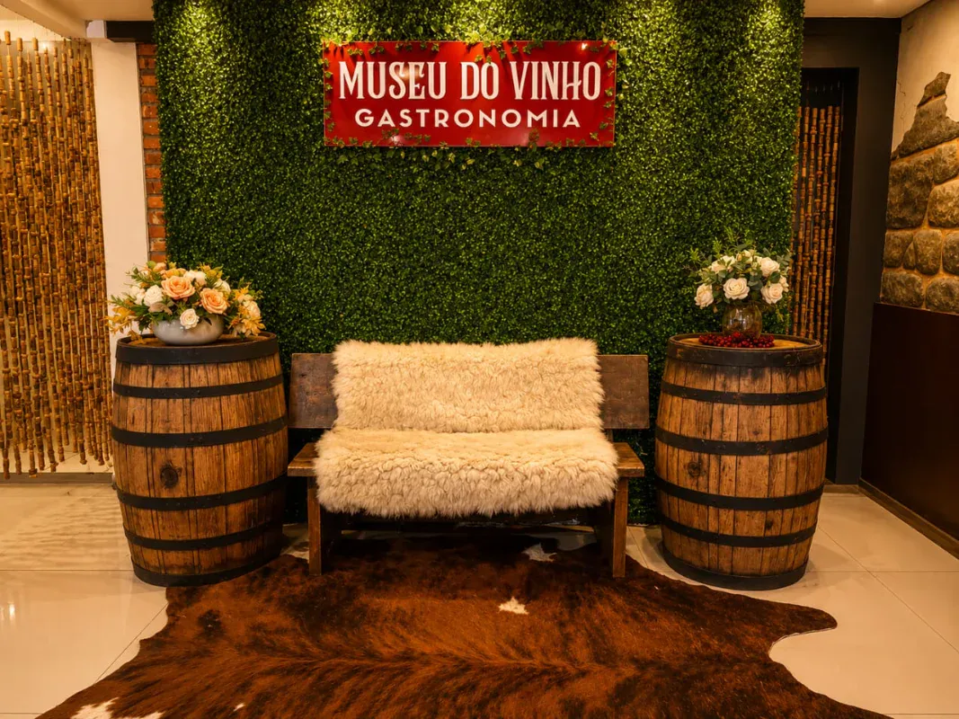 Recepção do Museu do Vinho Gramado com barris, banco de pelego e letreiro na parede verde