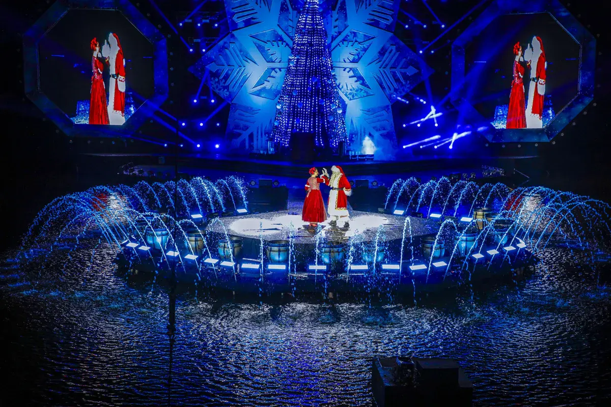 Fontes de água iluminadas e Papai e Mamãe Noel no palco do Nativitaten, no lago do Serra Park, em Gramado