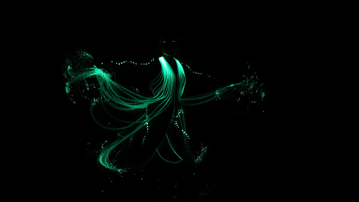 Bailarino gira com fios de luz verde espalhados pelo palco escuro, em apresentação da LightWire