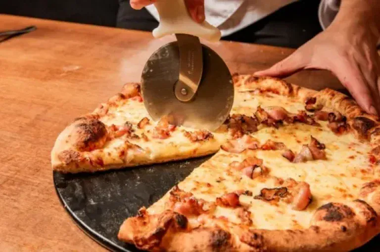 Pizza salgada sendo cortada com cortador de pizza na mesa da Pizzaria Fra Noi, em Canela