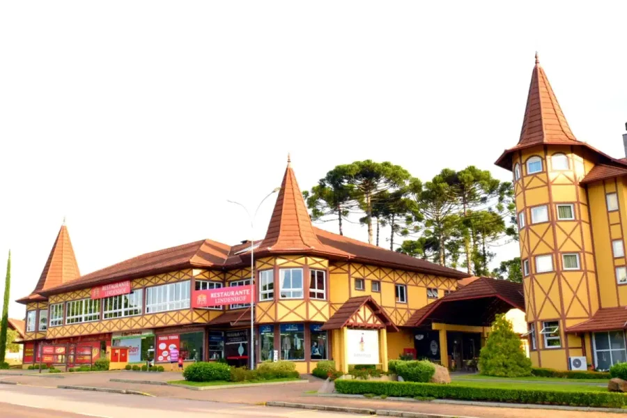 Fachada amarela em estilo colonial do Restaurante Lindenhof, com araucárias ao fundo, em Nova Petrópolis